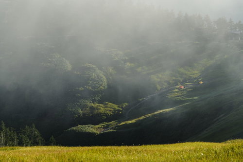夕日に照らされるテントと輝く草紅葉が広がる巻機山の山間