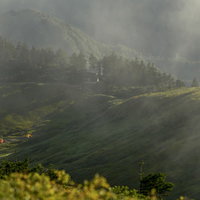 流れる雲の向こうに見える巻機山の避難小屋とテントの写真