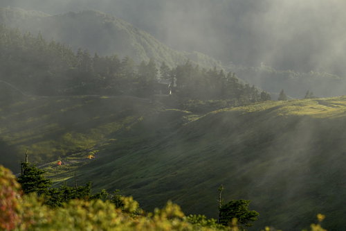 流れる雲の向こうに見える巻機山の避難小屋とテント