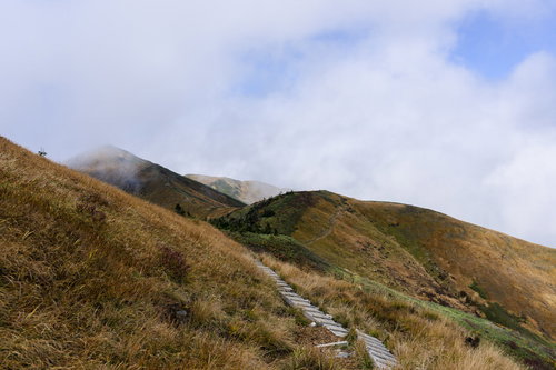 雲が飛び交う秋の巻機山稜線、木道と茶色く色づいた草原