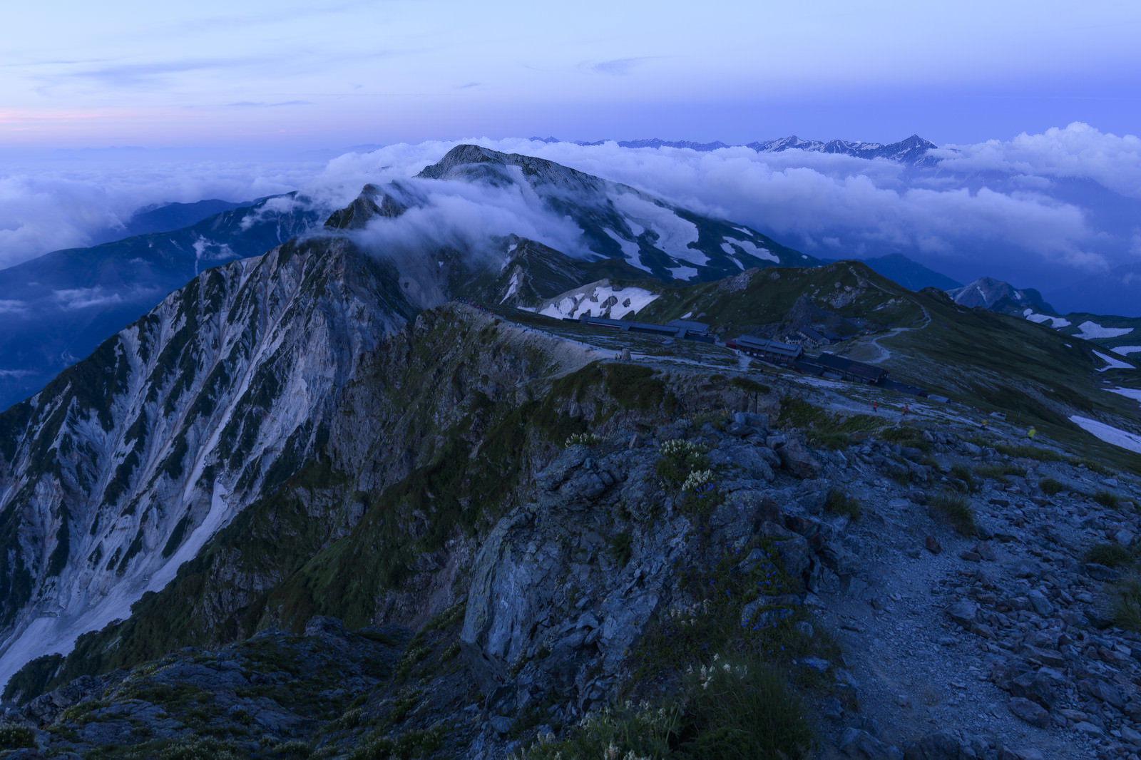 夜明けの薄明の中、白馬岳の険しい稜線に佇む山小屋と雲海の風景