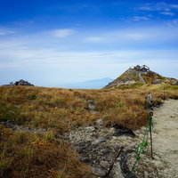 青空の下、黄色い枯草に覆われた月山山頂の秋の風景の写真