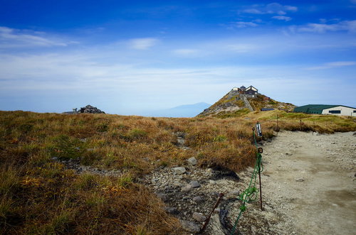 青空の下、黄色い枯草に覆われた月山山頂の秋の風景
