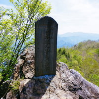 両神山山頂の岩場に立つ黒い石碑と新緑の山々の写真