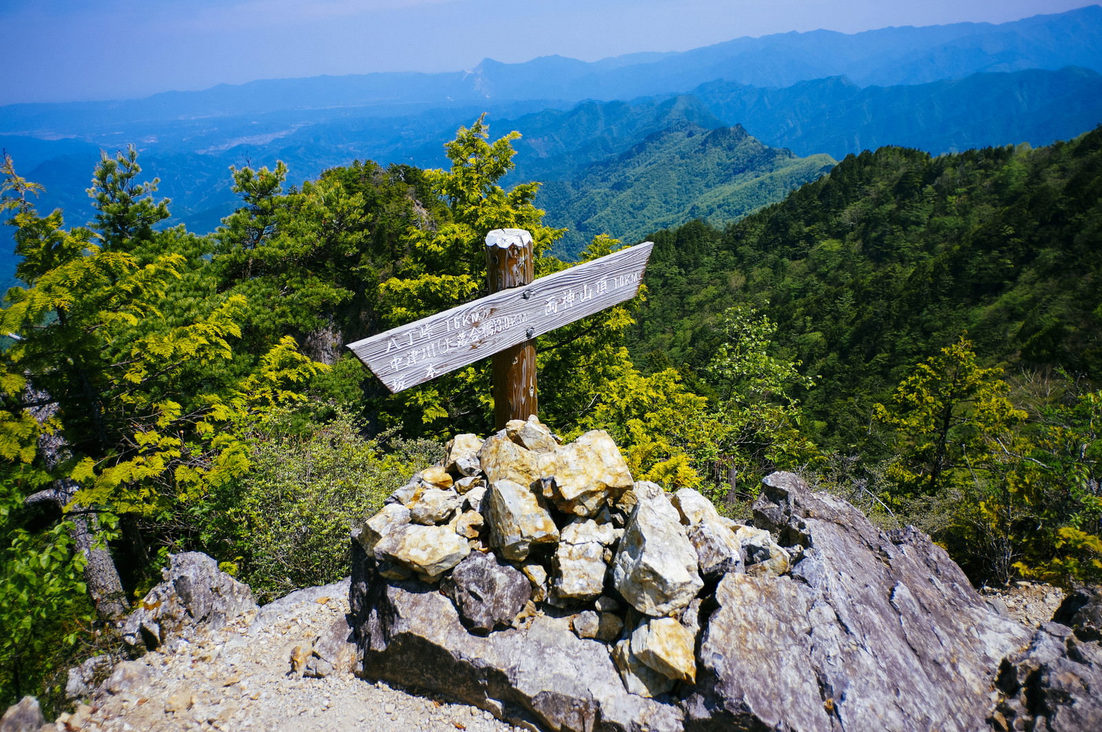 両神山の稜線に立つ白い指導標と青空、緑の山々の風景