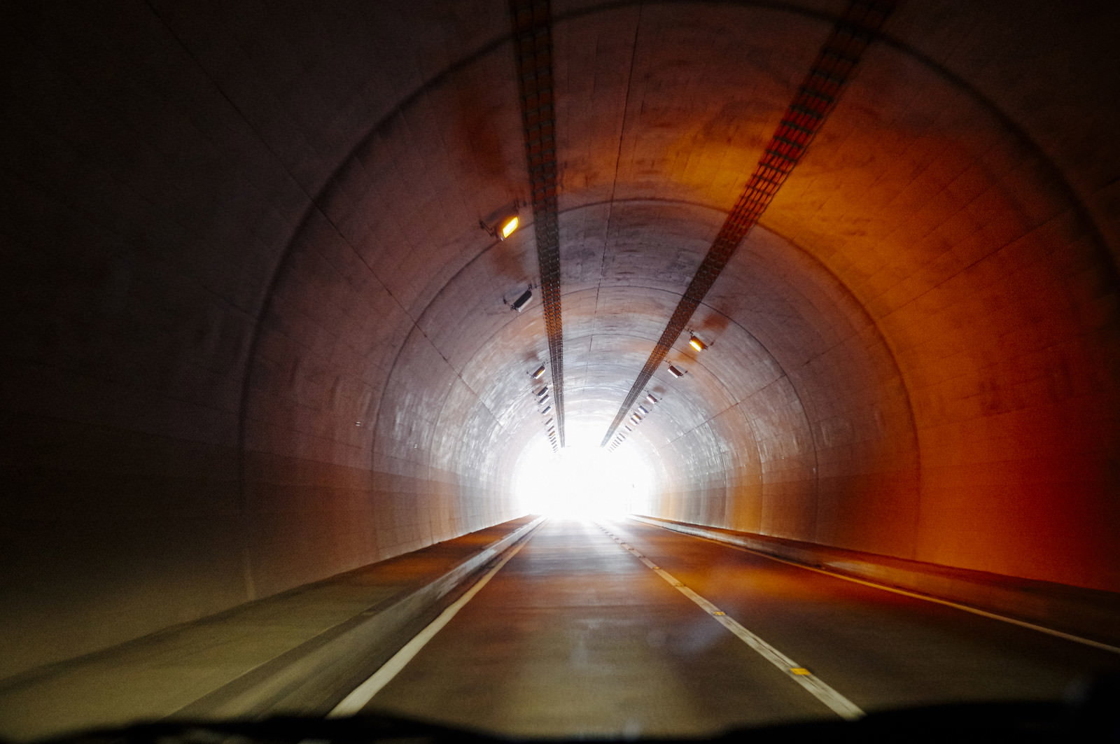 暗いトンネル内からオレンジ色の照明に照らされた道路と明るい出口が見える八丁峠へのトンネル