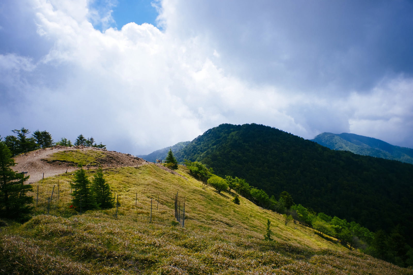 雲間から光が差し込む大菩薩嶺の稜線と緑の草原が広がる登山道