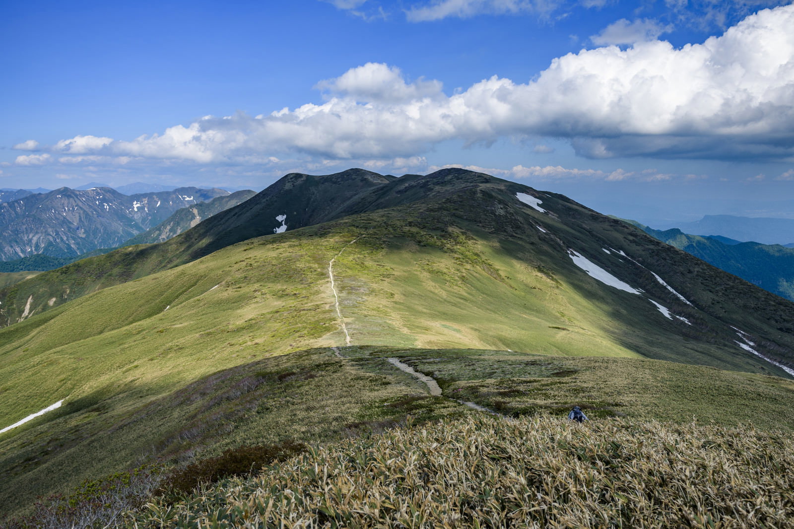 青空を背景に、緑の稜線を貫く登山道が奥へ続く。奥行きのある山岳風景