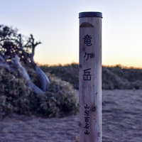 朝焼けの中、富士山を拝む竜ヶ岳山頂の登山者と碑の写真