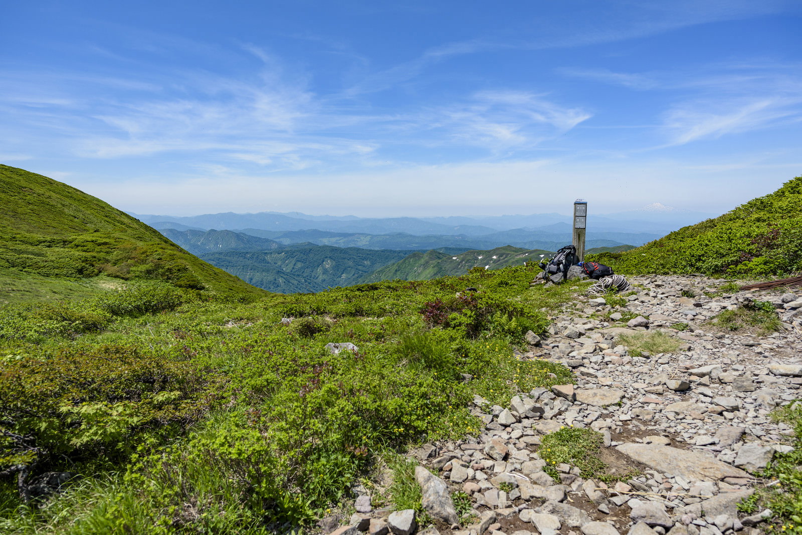 緑豊かな山並みを背景に登山道脇に置かれたリュックサック
