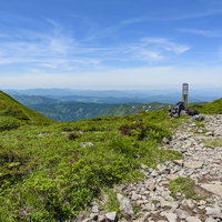 緑の山々を背景にした登山道脇にデポされたリュックの写真