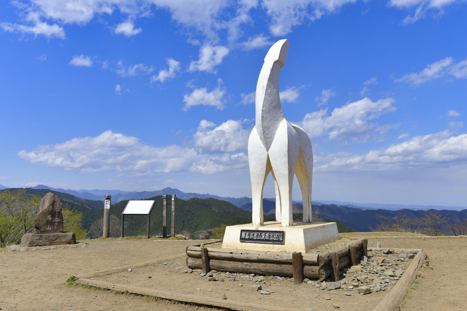 青空の下の山頂広場に設置された白いオブジェと記念碑
