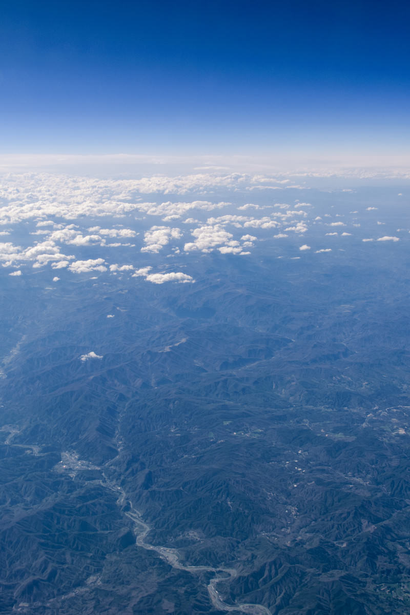 飛行機の窓から見える青空と雲、眼下に広がる大地の風景