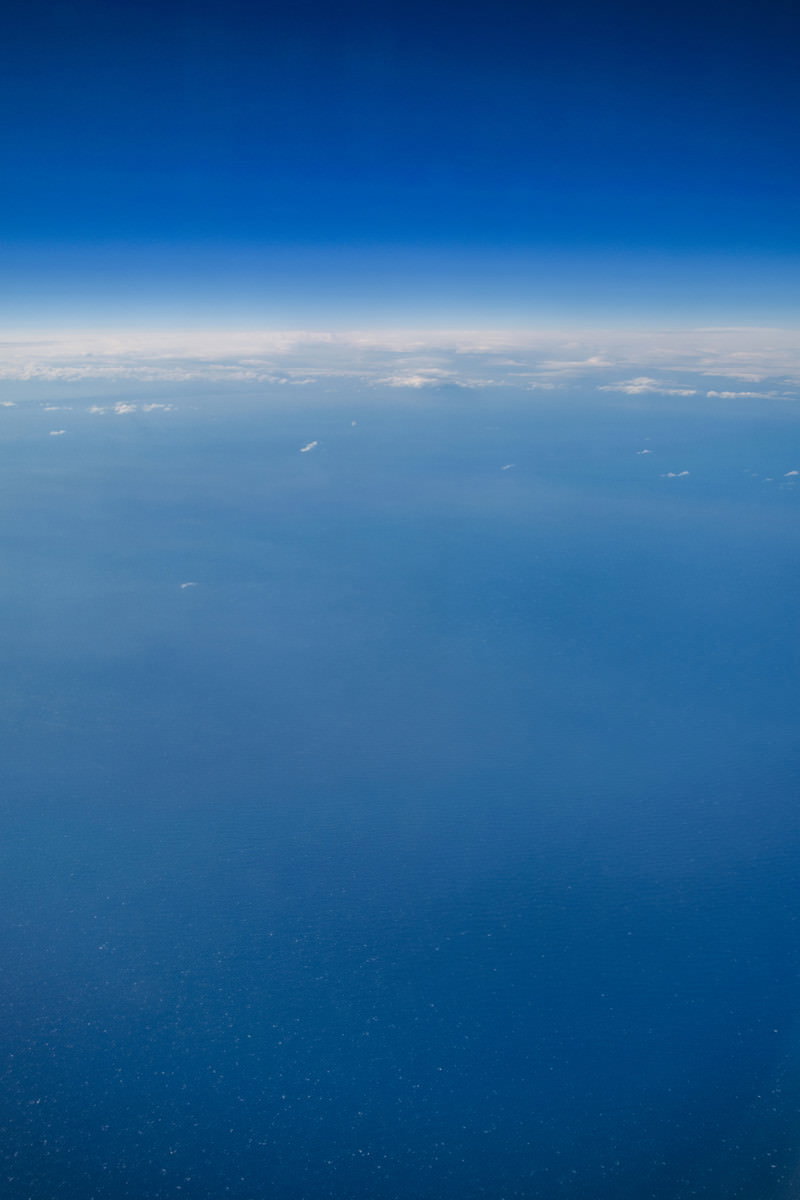 飛行機から見下ろした深い青色の海と澄んだ青空が水平線で分かれる上空からの眺め