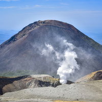 青空の下に立ち上る噴煙と阿寒富士の火山地帯の写真