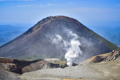 青空の下に立ち上る噴煙と阿寒富士の火山地帯
