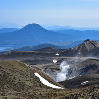 火山から沸き立つ蒸気と雄阿寒岳の山並みの写真