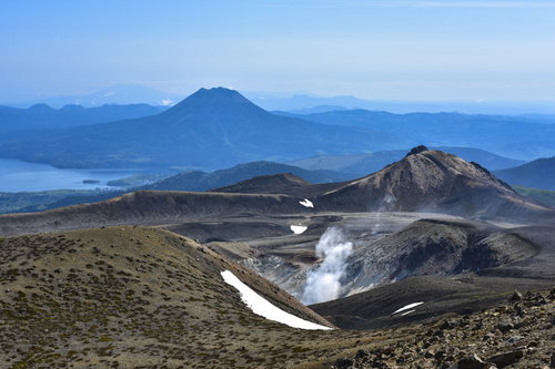 火山から沸き立つ蒸気と雄阿寒岳の山並み