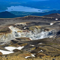 雌阿寒岳の火口から立ち上る噴煙と阿寒湖周辺を一望する景色の写真