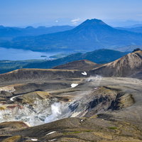 噴煙をあげる雌阿寒岳の火口と阿寒湖周辺を一望する景色の写真