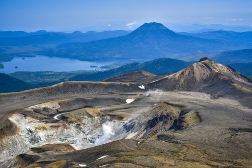 噴煙をあげる雌阿寒岳の火口と阿寒湖周辺を一望する景色