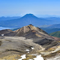 火口から噴煙が立ち上る雪が残る雄阿寒岳の火山風景の写真