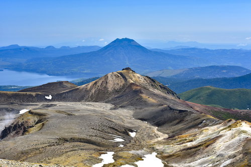 火口から噴煙が立ち上る雪が残る雄阿寒岳の火山風景