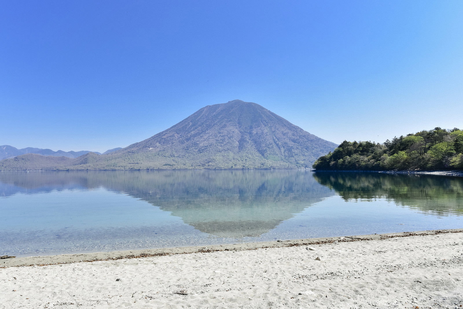 中禅寺湖の白い砂浜から眺めた男体山と湖面に映る水鏡の風景