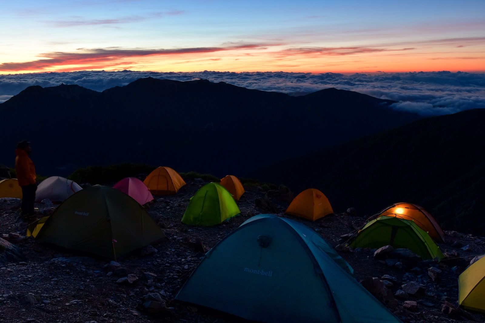 夜明けの空の下、山頂に設営されたテントと眼下に広がる雲海