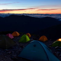 ご来光を待つテントたちと雲海の山頂キャンプの写真