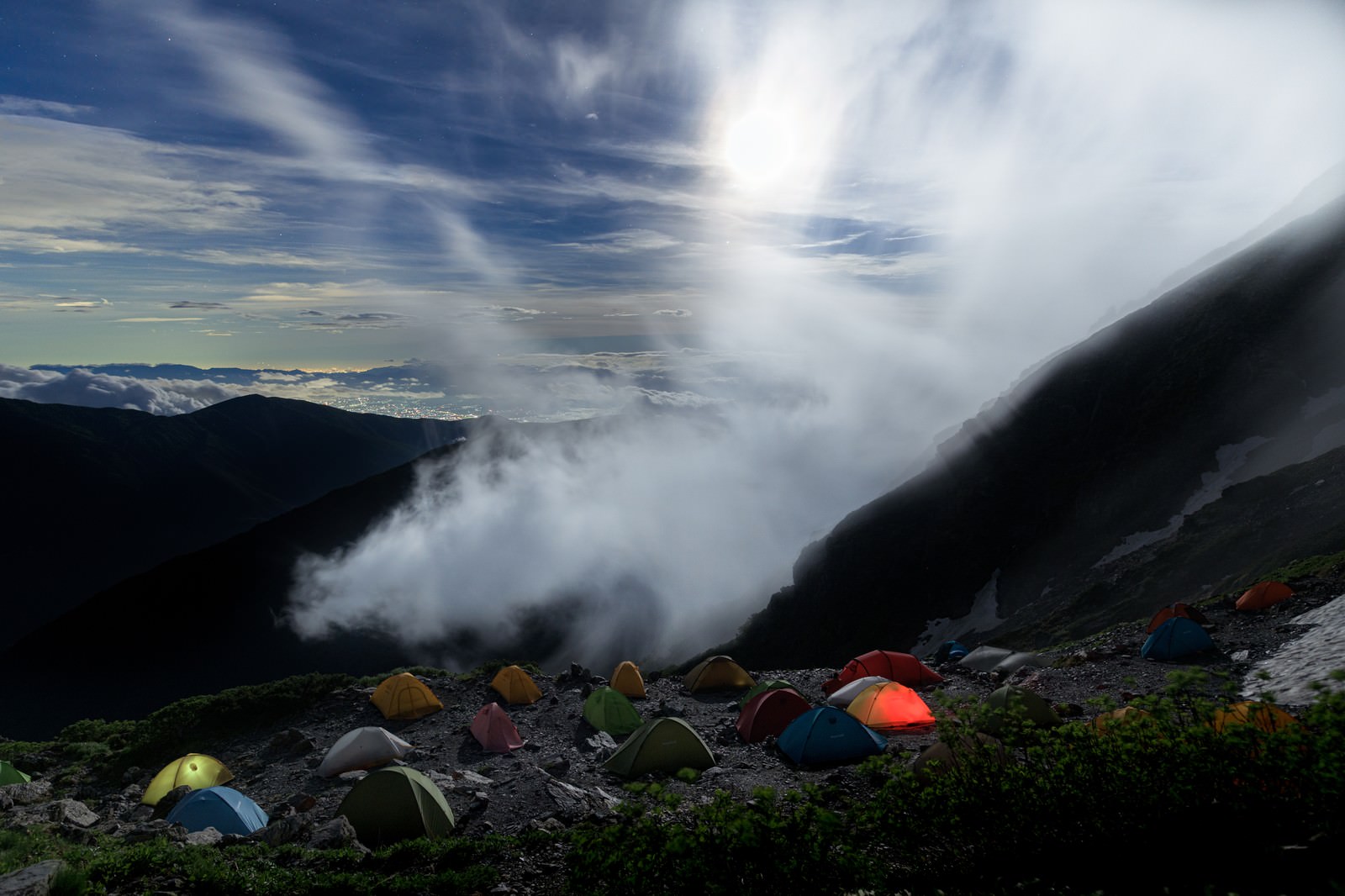 雲海の上に設営された複数のテントと朝日に照らされた山々の風景