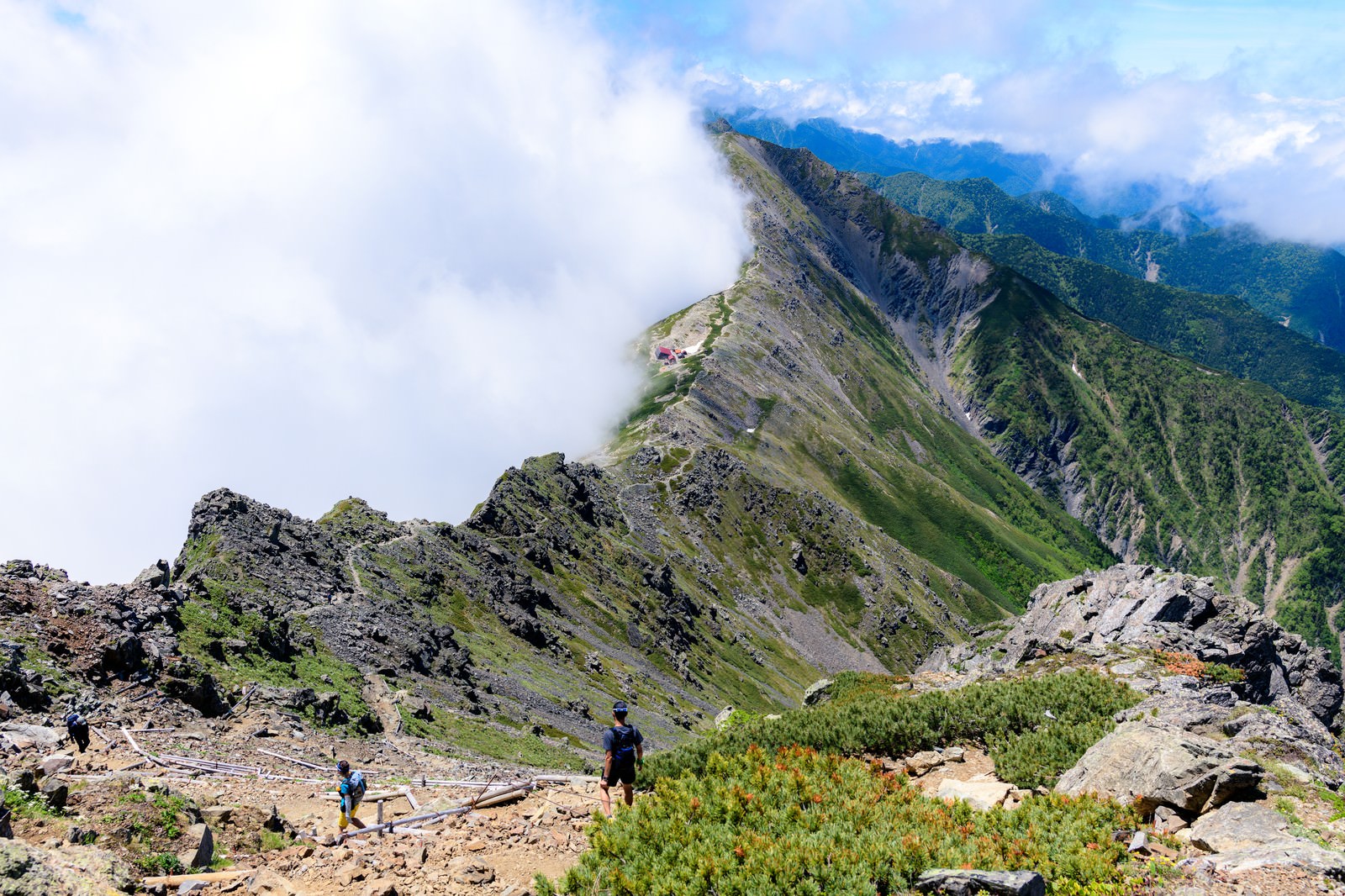 雲海に包まれた北岳の稜線で登山道を歩く登山者たち