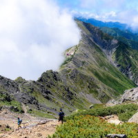 晴れと雲に分かれた北岳の稜線を行く登山者たちの写真
