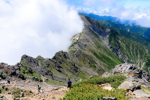 晴れと雲に分かれた北岳の稜線を行く登山者たち