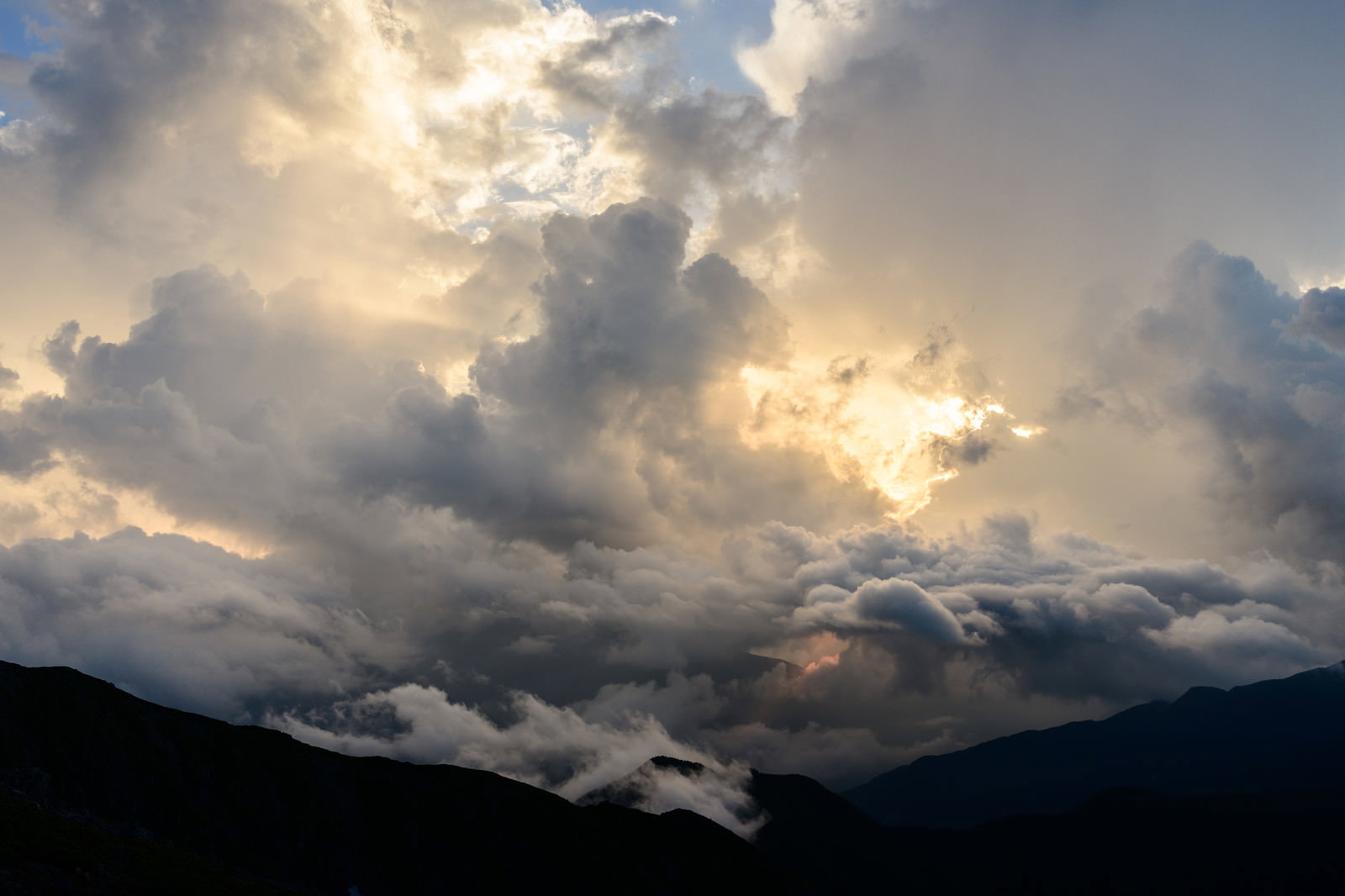 夕日に照らされてオレンジ色に染まった雲と暗いシルエットの山並み