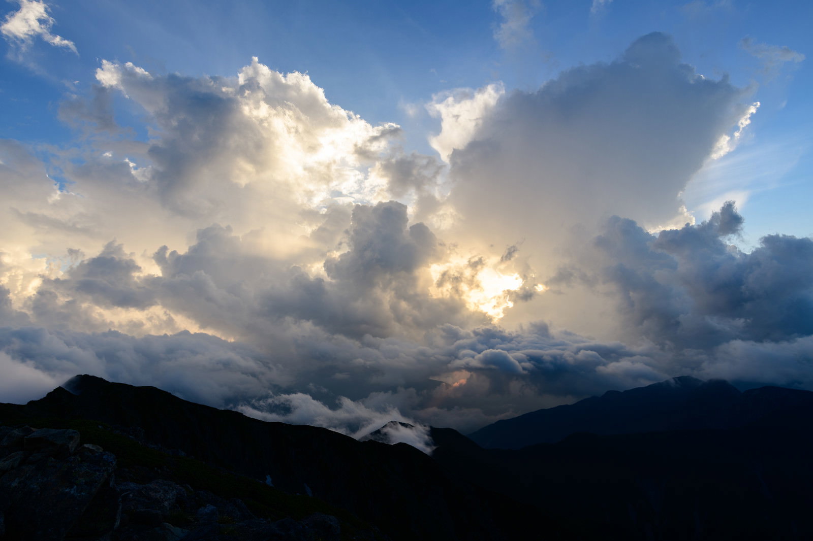 厚い雲の合間から差し込む太陽光が山脈を照らす風景