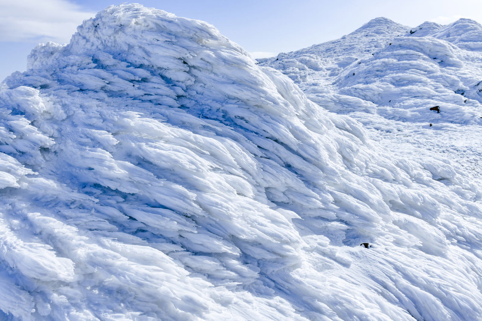 雪と樹氷に覆われた山の斜面で波打つような雪の模様