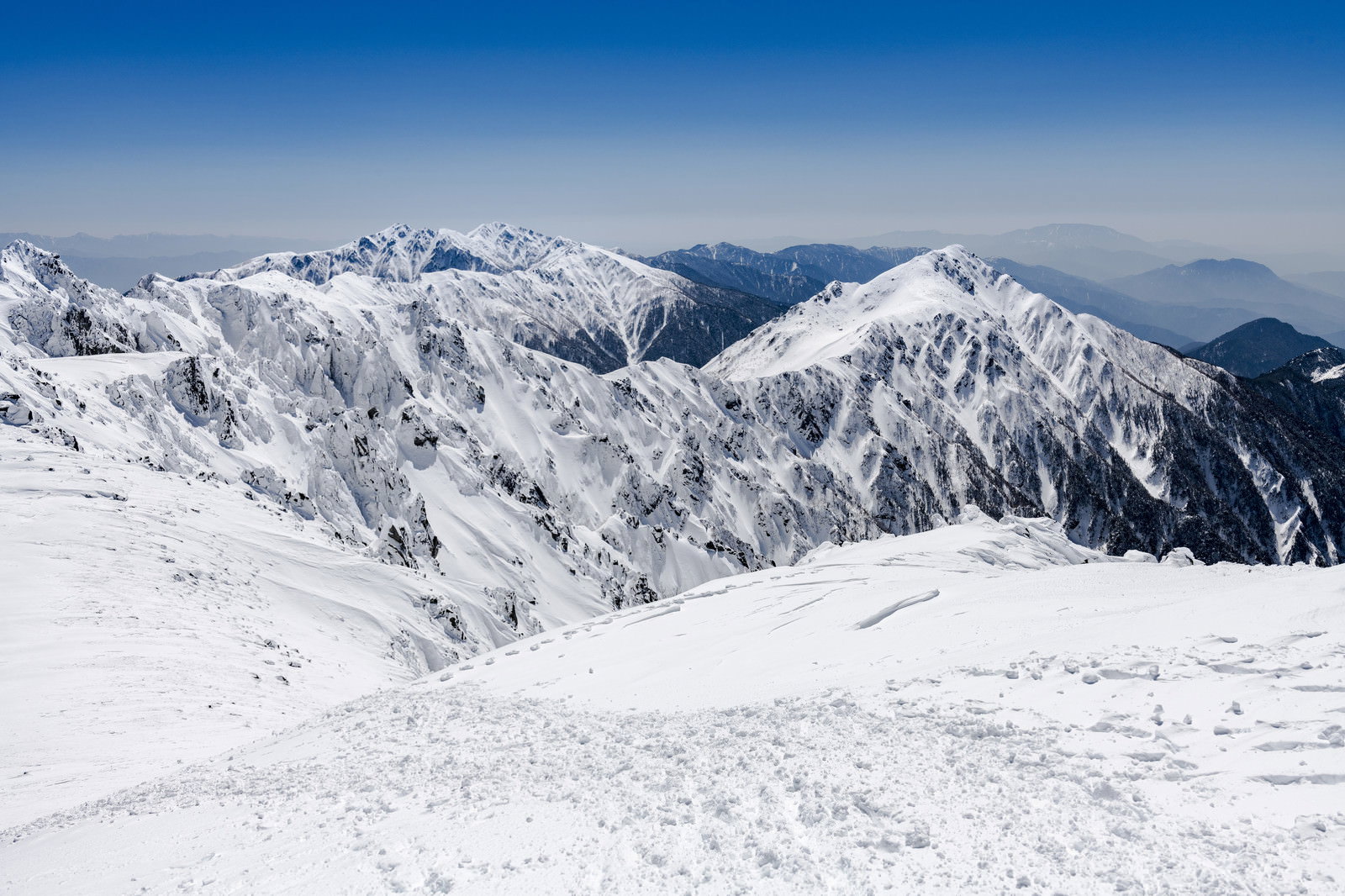 青空の下に雪化粧した中央アルプスの稜線が連なる冬山の風景