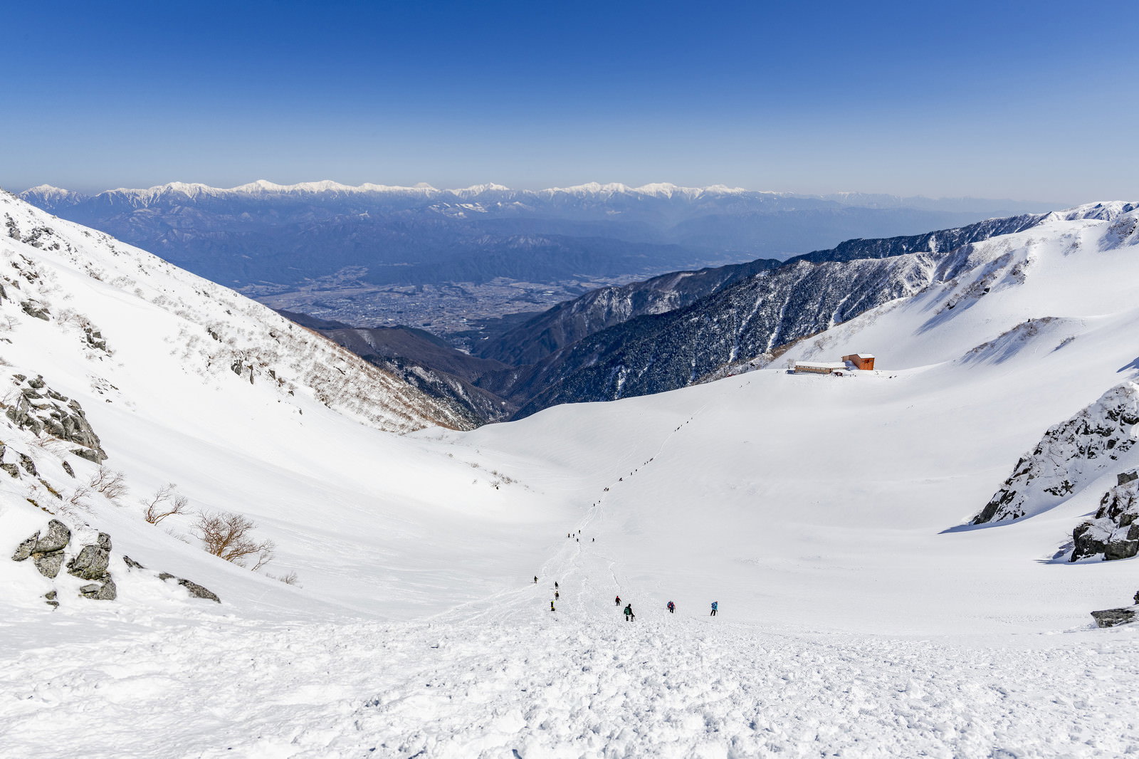 雪に覆われた千畳敷カールの斜面を歩く登山者たちと遠方の雲海