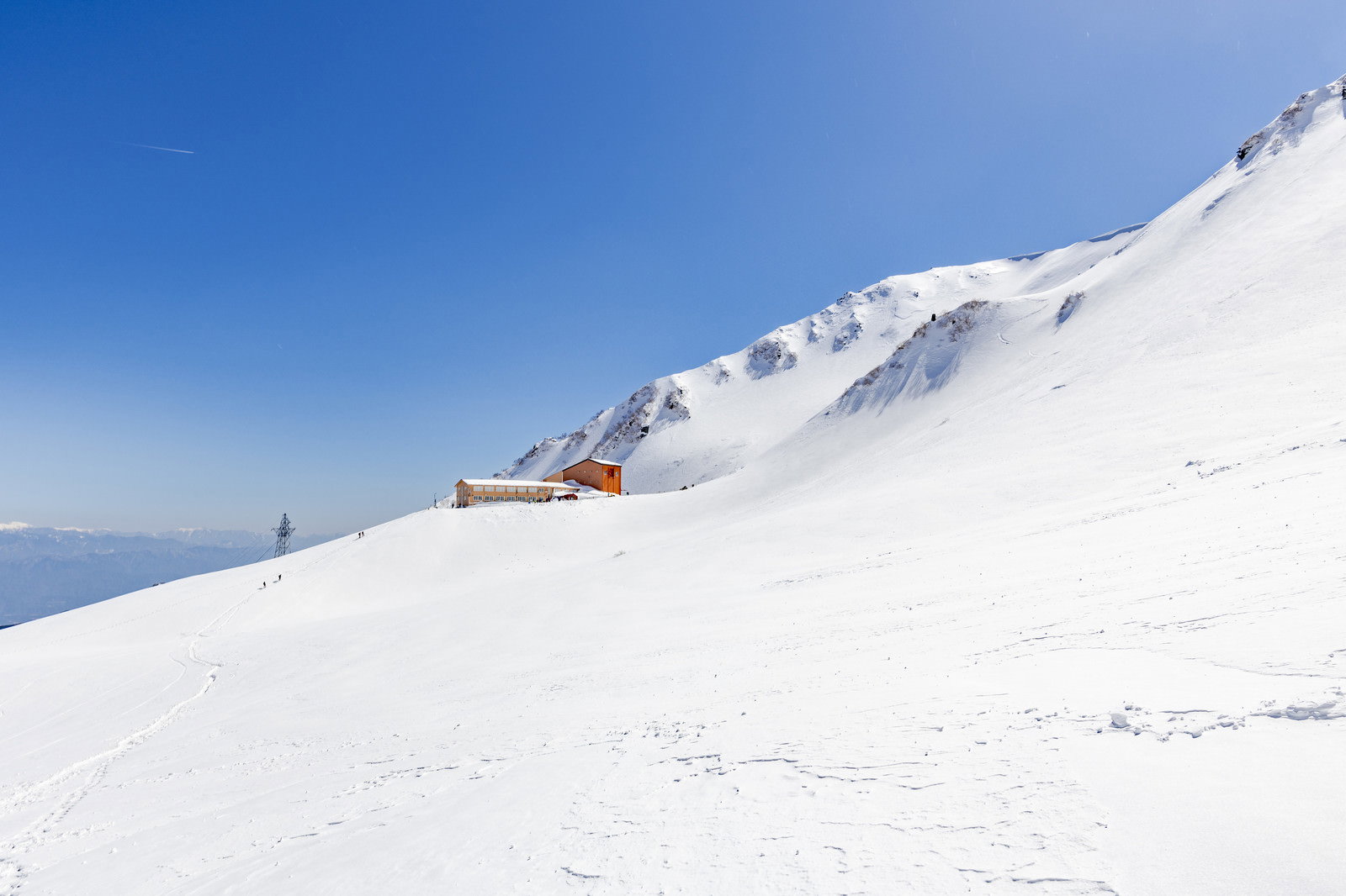 雪山の斜面に建つオレンジ色の千畳敷ホテル、青空が広がる冬の木曽駒ヶ岳