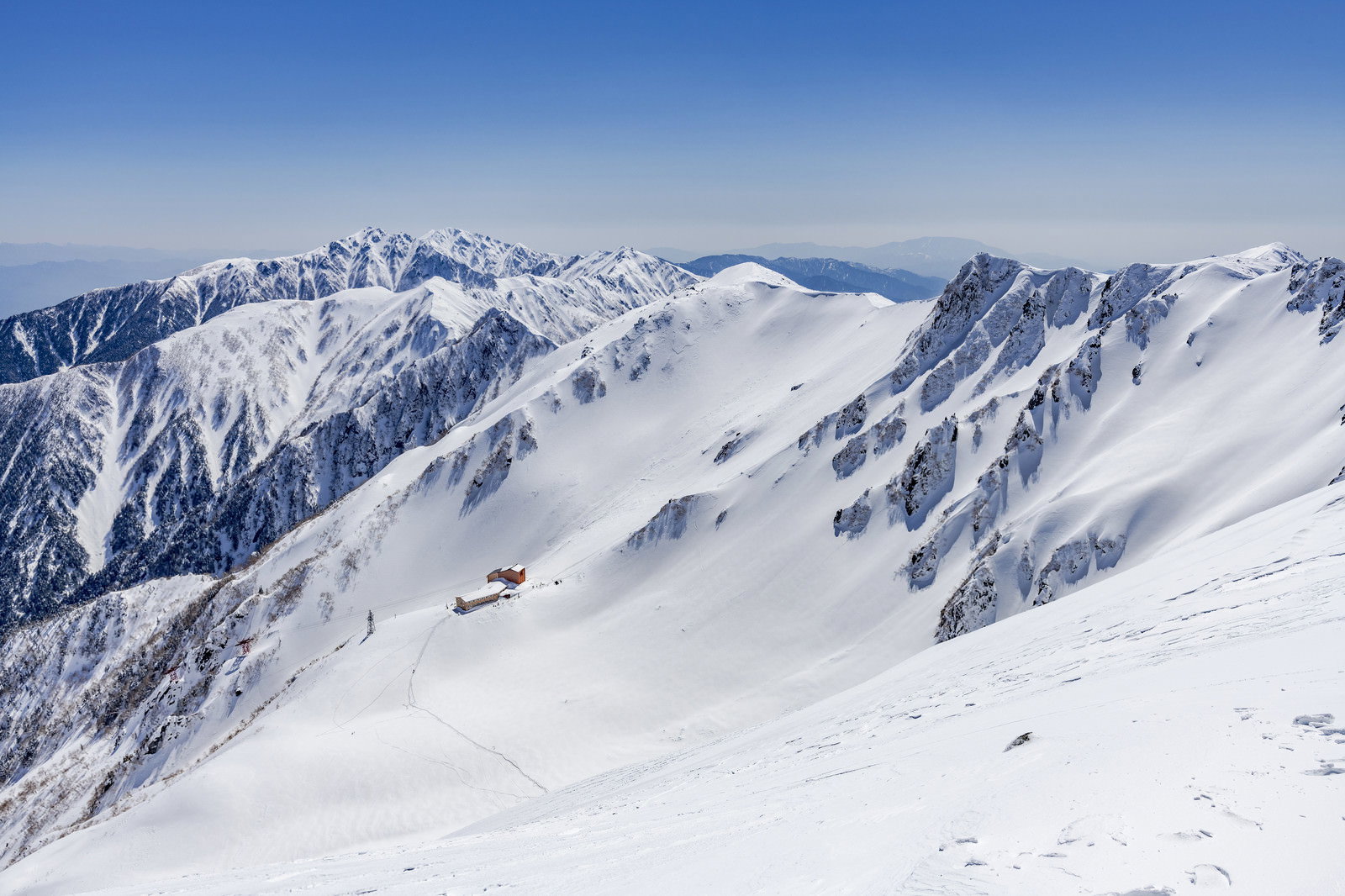 雪に覆われた千畳敷カールの斜面に建つホテル千畳敷と山々の稜線