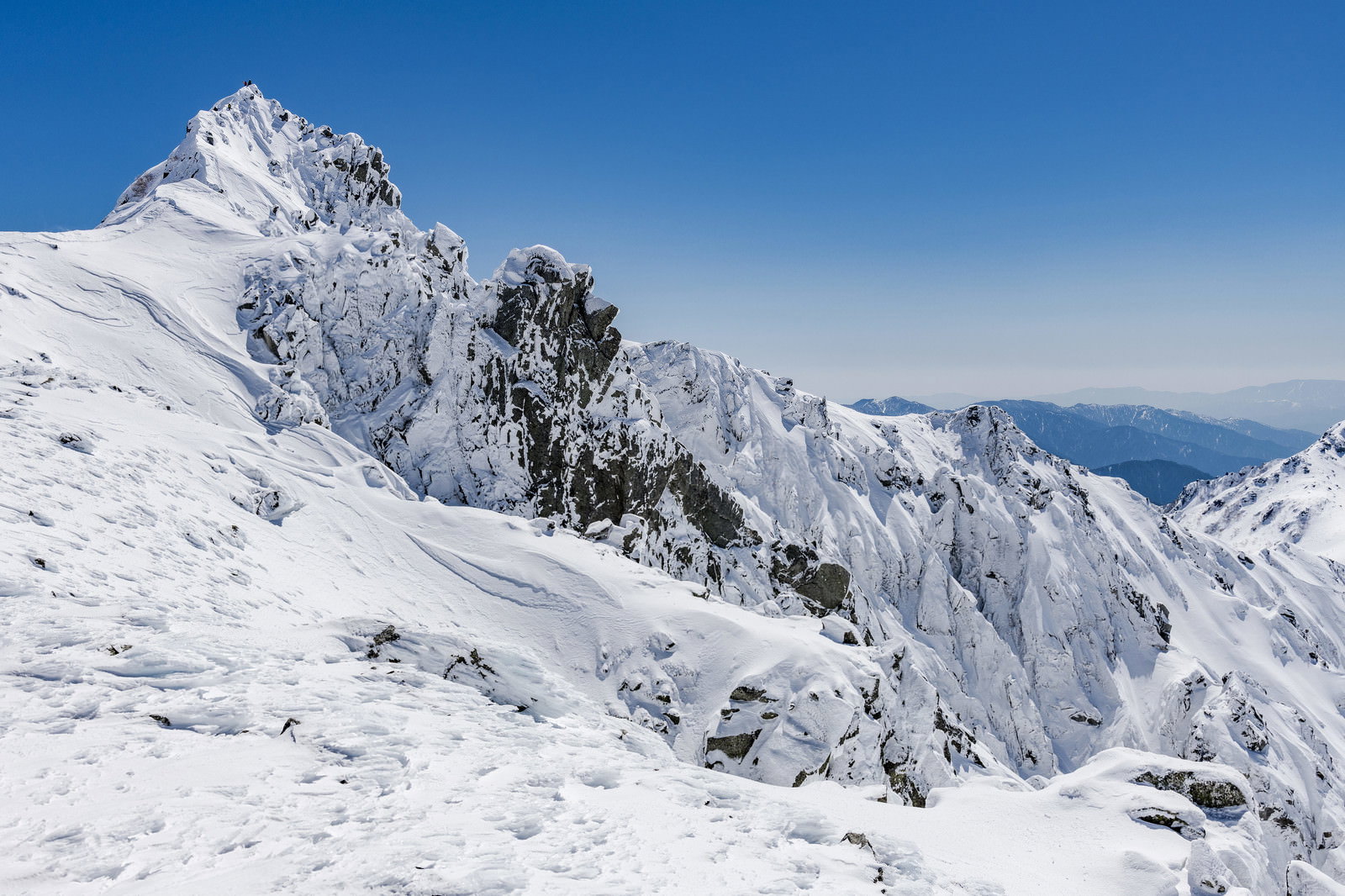 宝剣岳の岩峰頂上に立つ登山者と雪山の風景