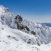 宝剣岳の岩峰の頂に立つ登頂者（木曽山脈の雪景色）の写真