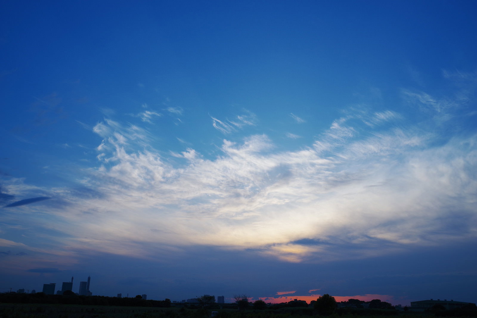 オレンジ色に染まった夕焼け空に雲が浮かび、地平線に夕日が沈む風景