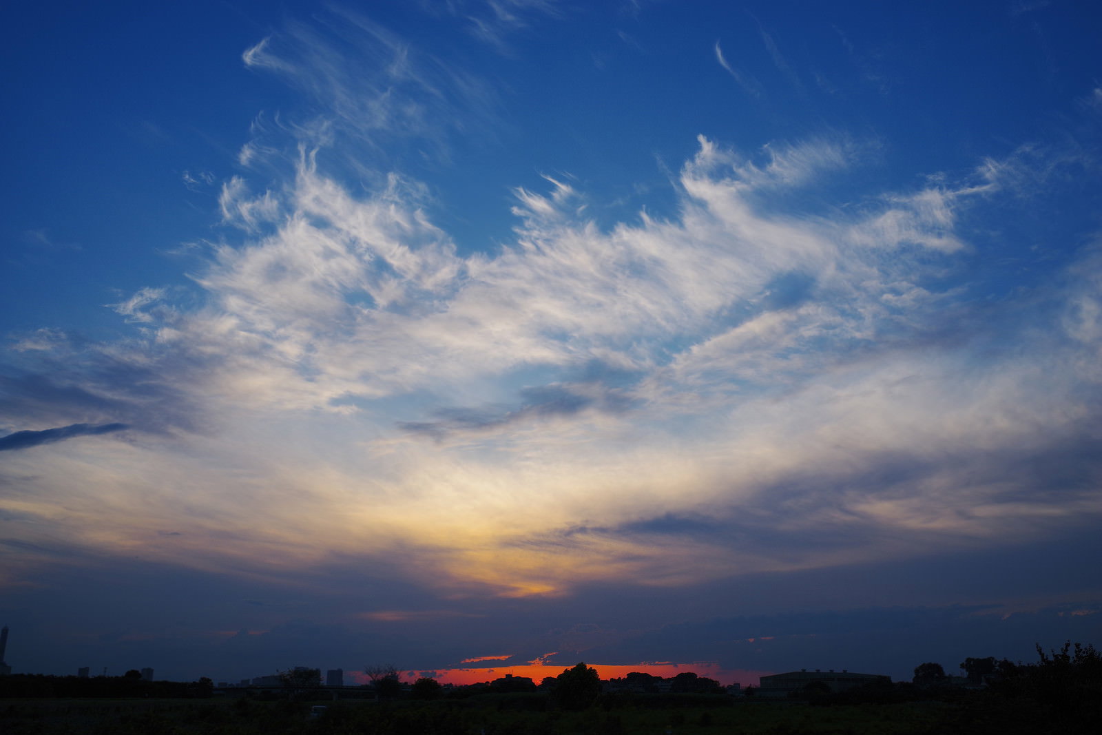 オレンジ色に焼けた地平線の上に青空と白い雲が広がる夕焼けの風景