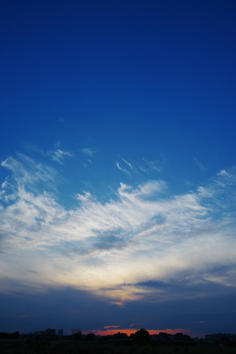 真っ青な空に白い雲が広がり、地平線にオレンジ色の夕日が輝く夕焼けの風景