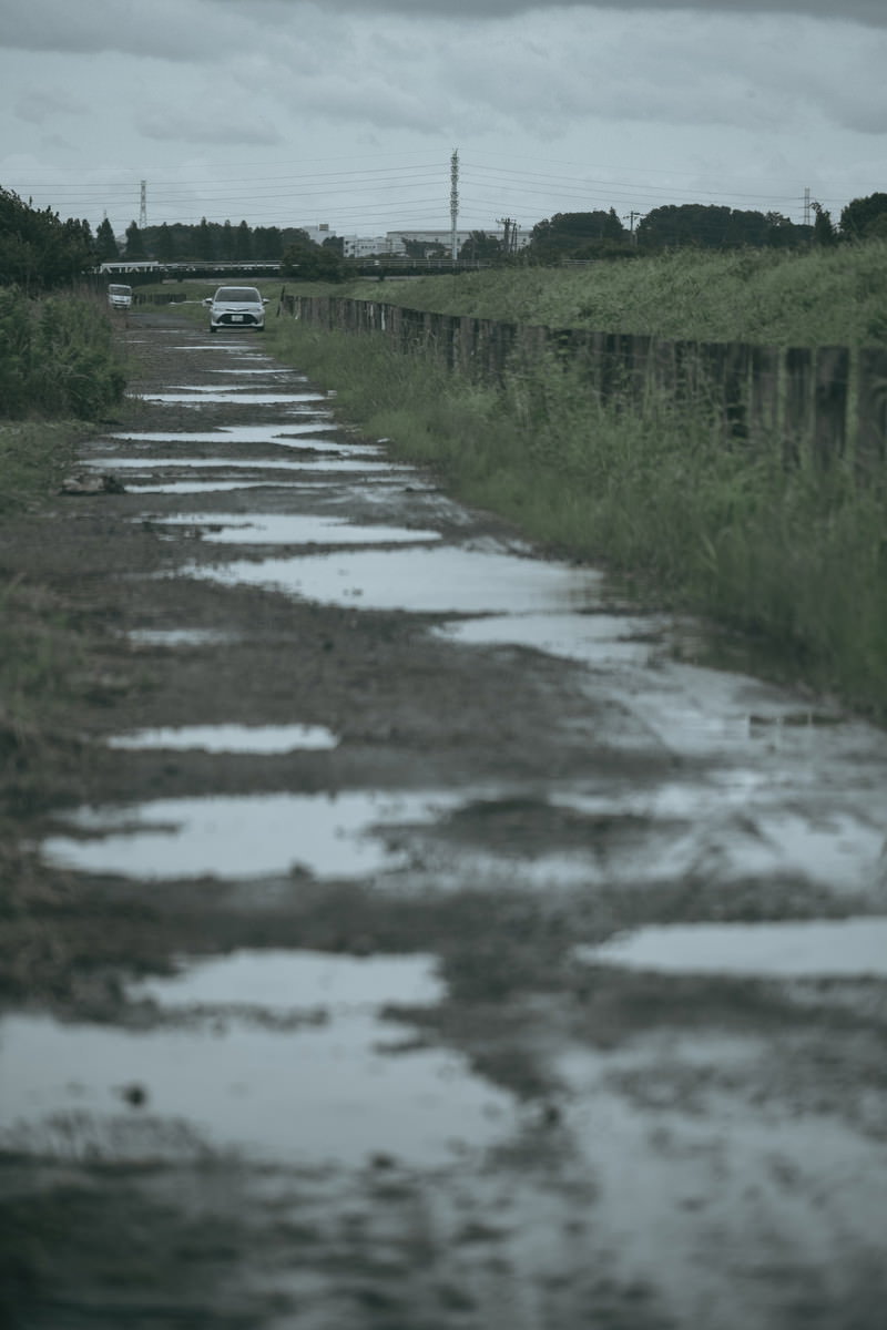 雨上がりの砂利道に点在する水溜りと曇り空