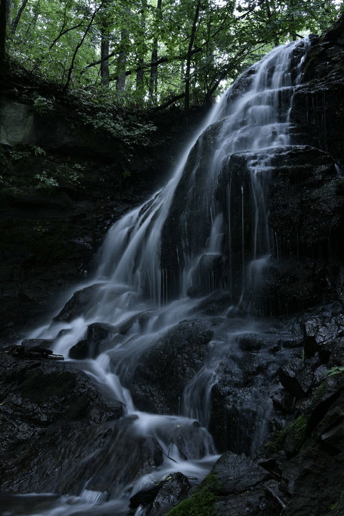 森の岩場を流れ落ちる冷ややかな滝と水飛沫