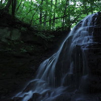 森林の中をひっそりと流れるトブシの滝と水飛沫の写真