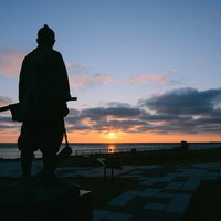 樺太を見つめる間宮林蔵像と夕焼け空の写真